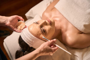 Beauty parlor beautician hands applying mask to female client face with brush